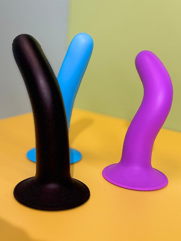 Three silicone toys in black, blue, and purple on a yellow surface with a gray and green background.