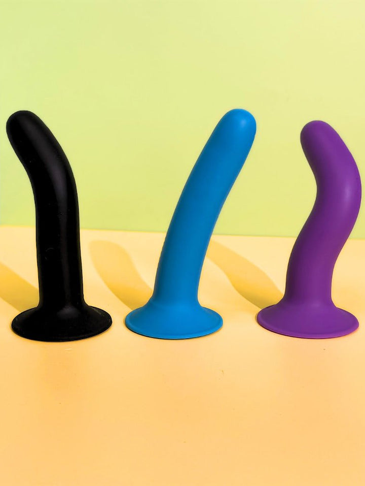 Three silicone toy in black, blue, and purple on a yellow surface with a green background.