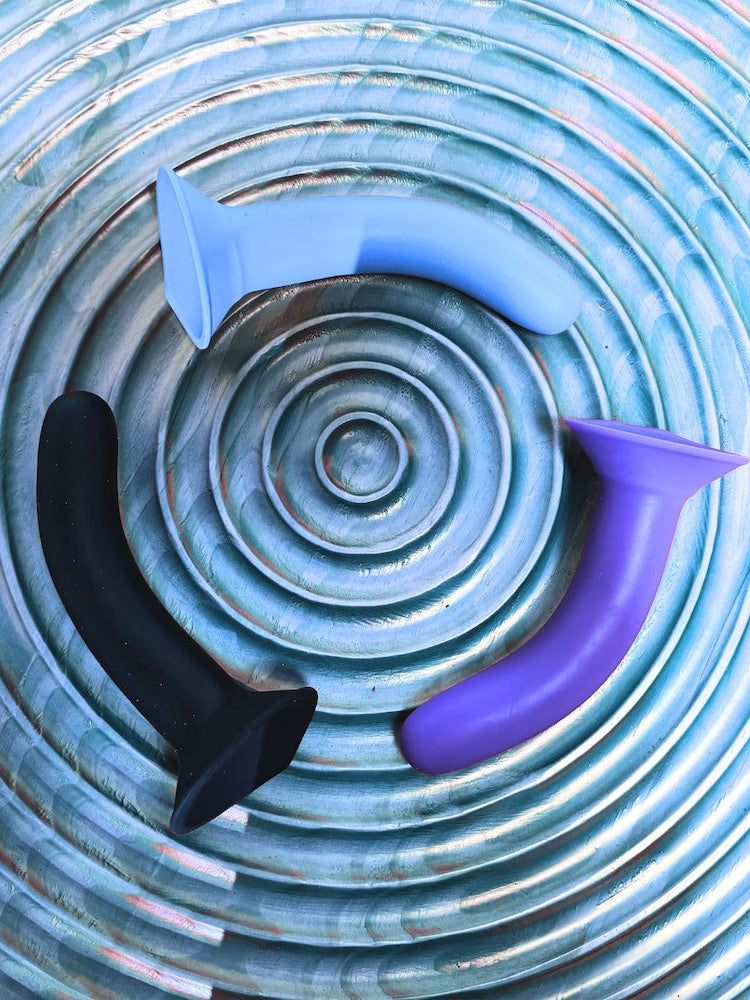 Three silicone toys in black, purple, and blue on a textured blue surface.