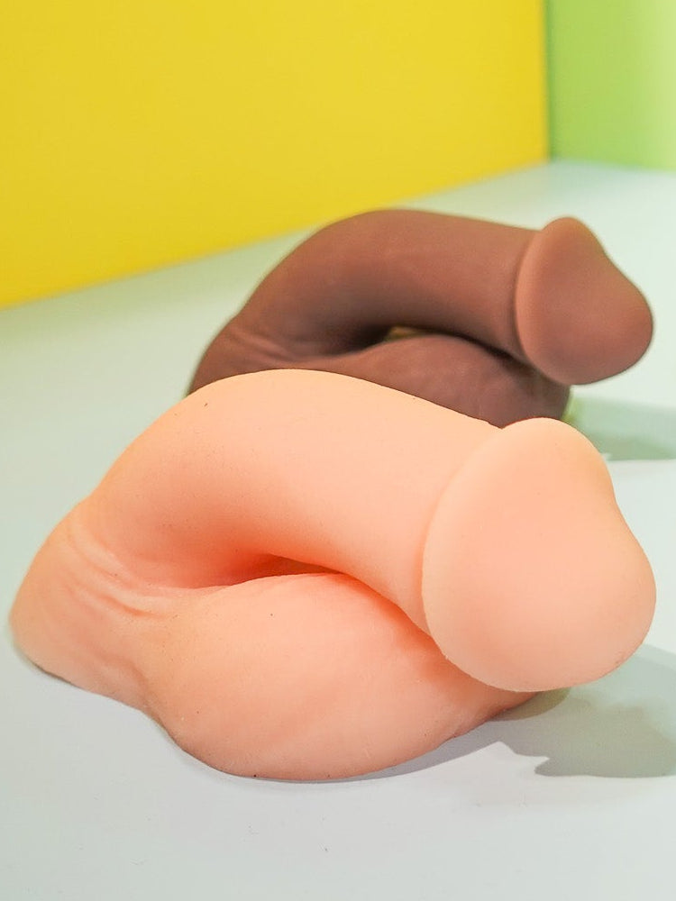 Three silicone butt-shaped toys on a white surface with a yellow and green background