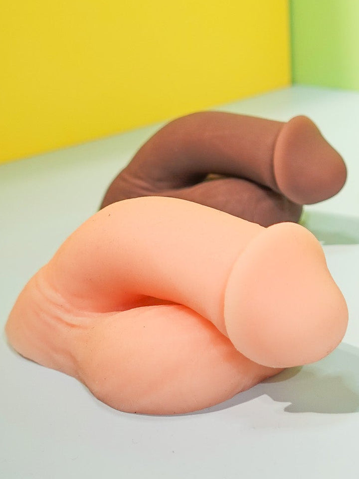 Three silicone butt-shaped toys on a white surface with a yellow and green background